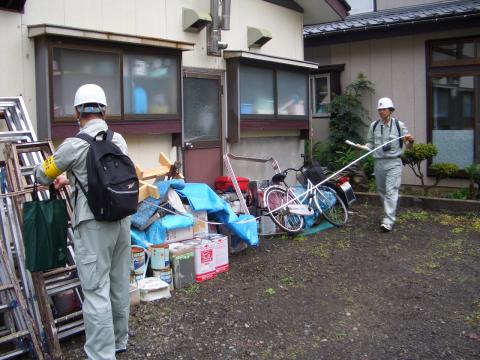 二人の作業員が家の前にロ0ぷを張っている写真