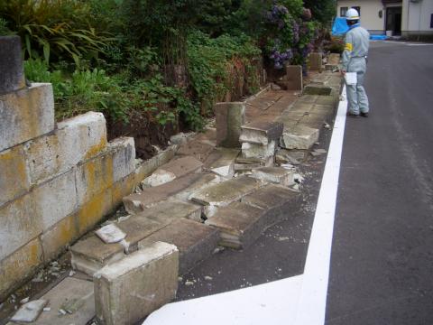 ブロック塀が崩れている前一人の作業員が立っている写真