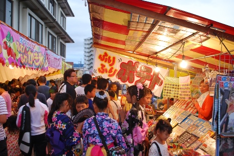 いろいろな屋台が並んでいるところにたくさんの大人や子どもが集まっている様子の写真