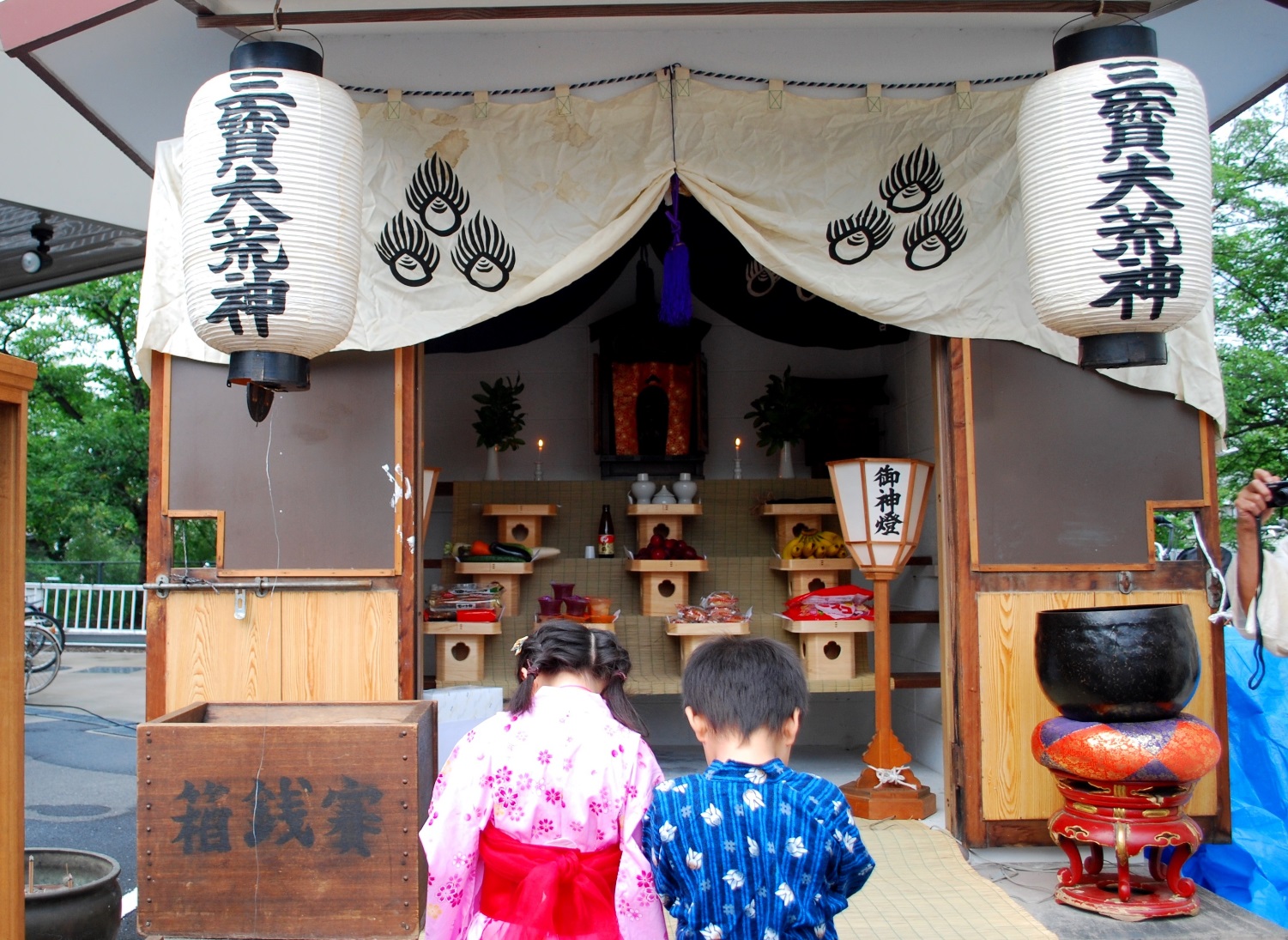 ピンクの浴衣を着た女の子と青い浴衣を着た男の子がすももの荒神さんに向かってお参りをしている様子の写真