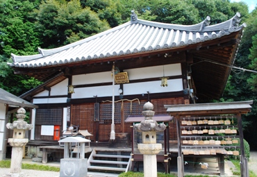 手前に灯籠が2つと絵馬掛所がある寺の本堂の写真