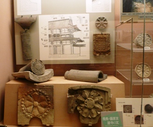 花のような模様が浮き出た土器が2つ並び、真上のボードに図解が貼られている展示の写真