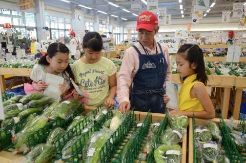 まほろばキッチンの職員が並べられた野菜を前に、小学生に説明をしている様子の写真