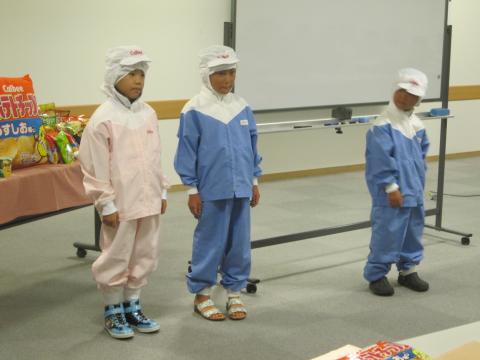 工場服の試着体験を行っている3人の小学生たちの写真