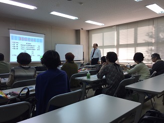 参加者がイスに座って正面にあるプロジェクトを見ながら講師から説明を受けている写真