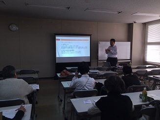 参加者がイスに座って前にあるプロジェクターを見ながら講師の話を聞いている写真