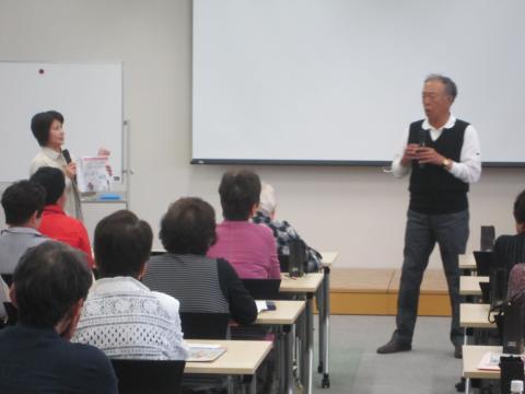 男性1名と女性1名がスクリーンの前でマイクを持って啓発劇を行っている写真