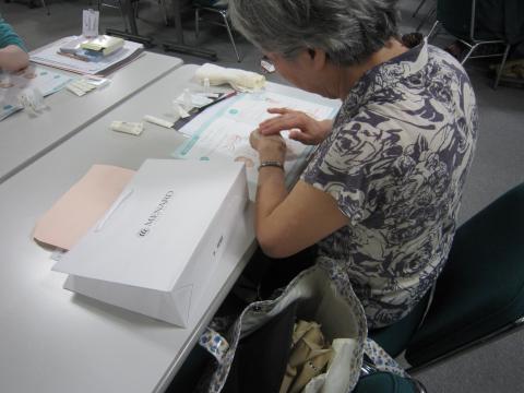 女性が1名下を向いて、左手に化粧品を縫っている写真