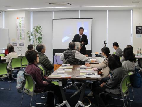 スクリーンの前で講演者1人がセミナー参加者に向かって話している写真