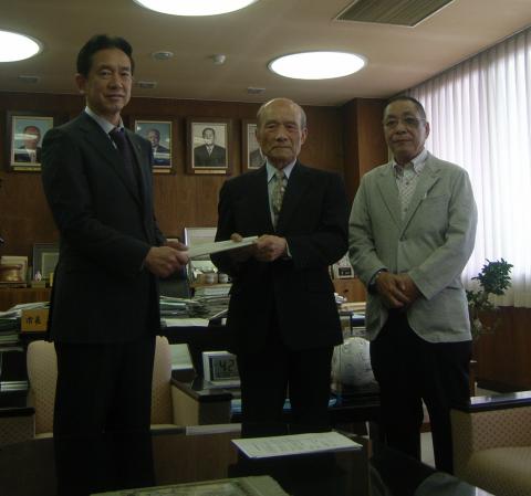亀田市長とその左側に並んで答申を持ちあっている川上会長と米田副会長の写真