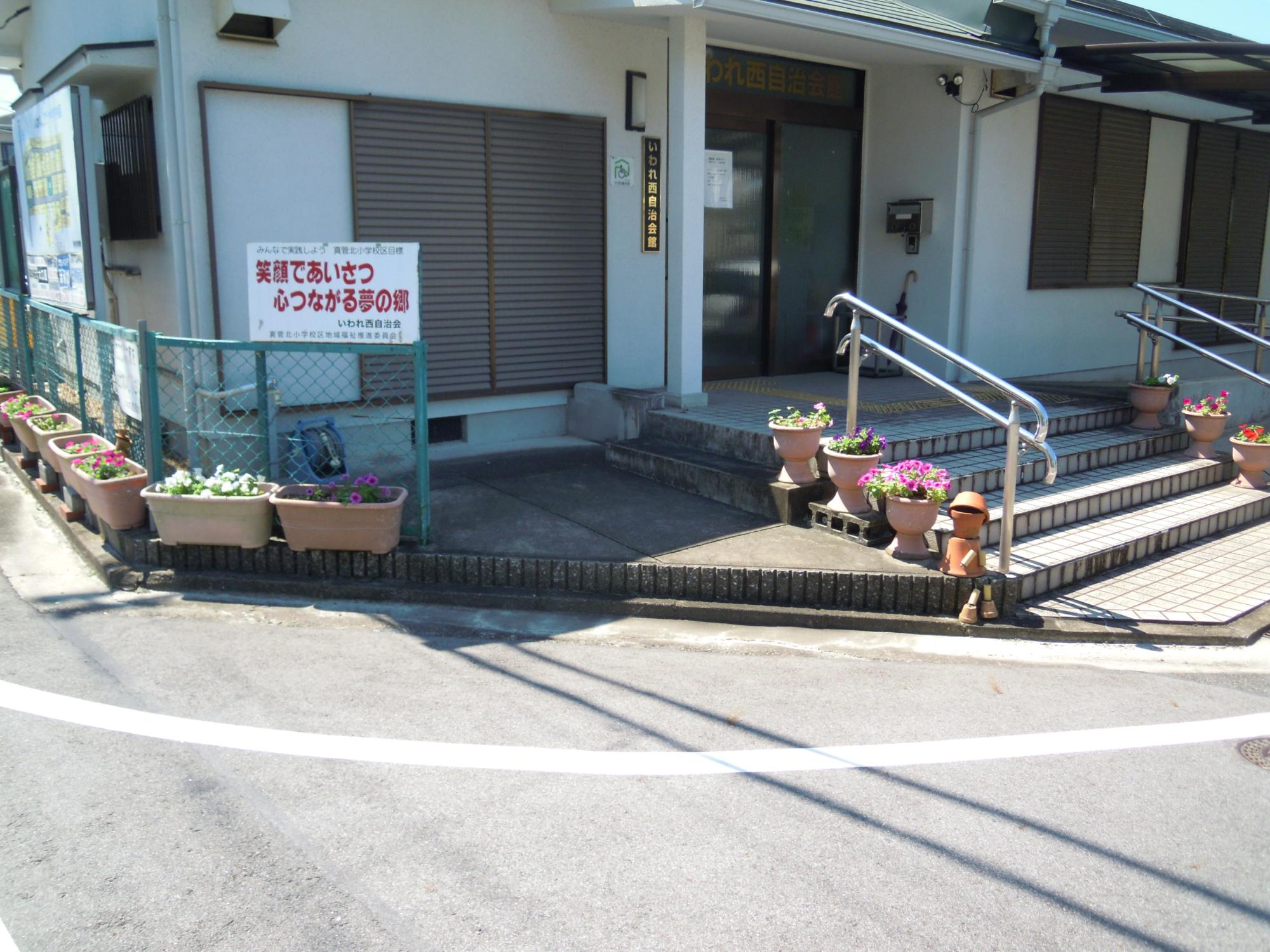 いわれ西自治会館前にある色とりどりの花が咲いている複数の植木鉢の写真