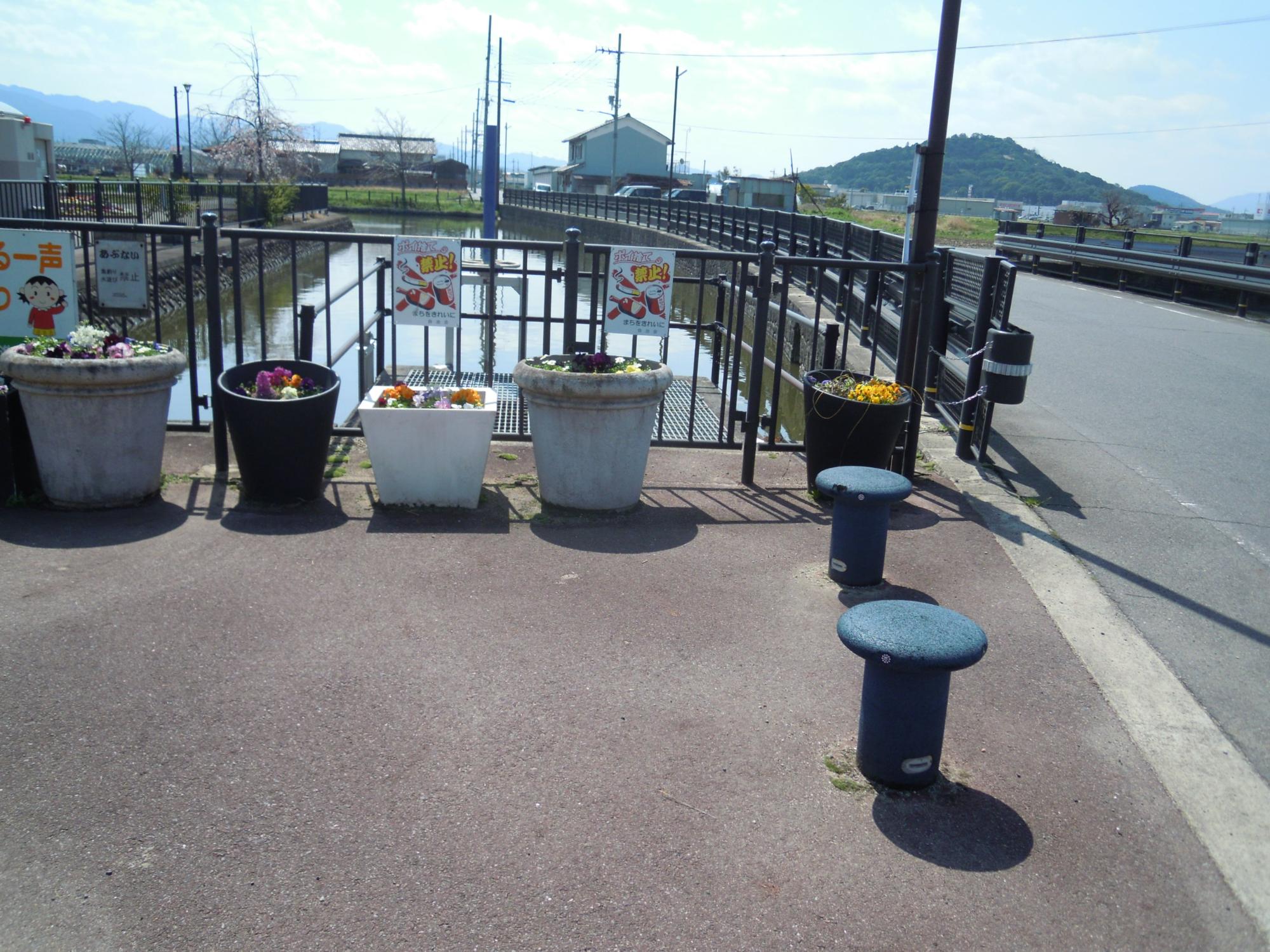 川の橋の上にある色とりどりの草花が咲いている植木鉢5個の写真