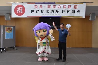 国内推薦を祝福する横断幕の下で記念撮影する橿原市長と観光PRキャラクター「さららちゃん」の写真