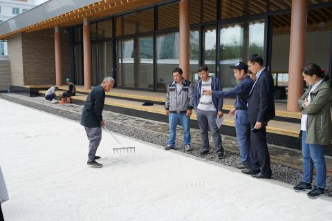 レーキを使い砂紋造形を指導する造園家の方とそれを見るナザルバエフ大学の施設管理担当者の皆さんの写真