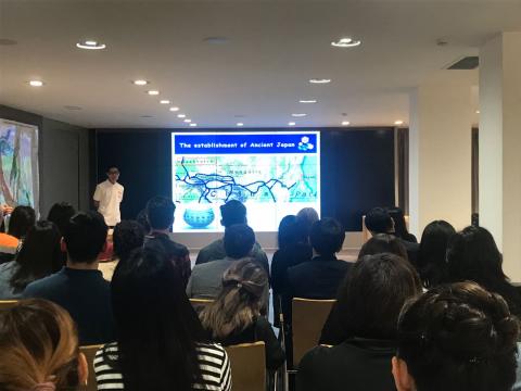 大きなスクリーンで行われる講演会と、それを聞いてる人々の写真