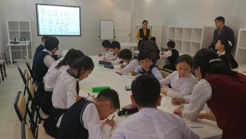 机を囲んで座り年賀状を作る子供達とそれを教える大人の写真