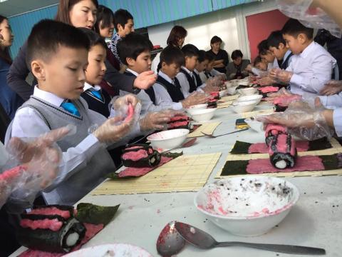 机を囲んで飾り巻き寿司を作る子供達の写真