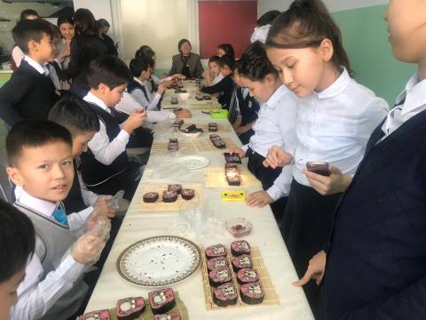 机を囲んで飾り巻き寿司にトッピングする子供達の写真