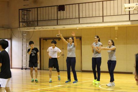 五人が一列に並んでいて真ん中の人が笑顔で手を上げている写真