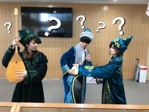 カザフの楽器を手に頭にはてなマークを浮かべるカザフの民族衣装を着た3人の写真
