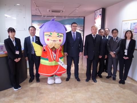 館内でのバウダルベック大使と市関係者複数名、およびマスコットキャラクターとの集合写真