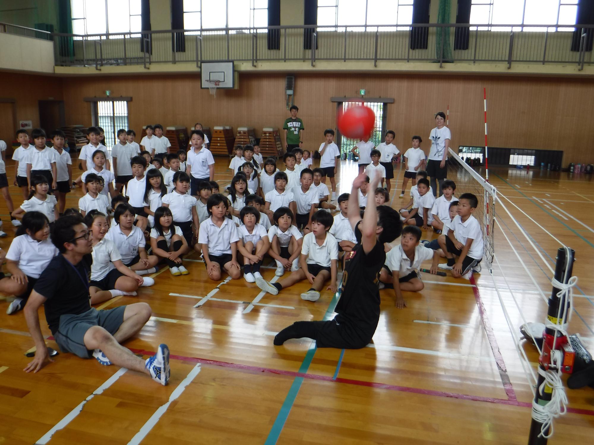 体育館で嵯峨根選手が大勢の生徒を前にボールを上に上げている写真
