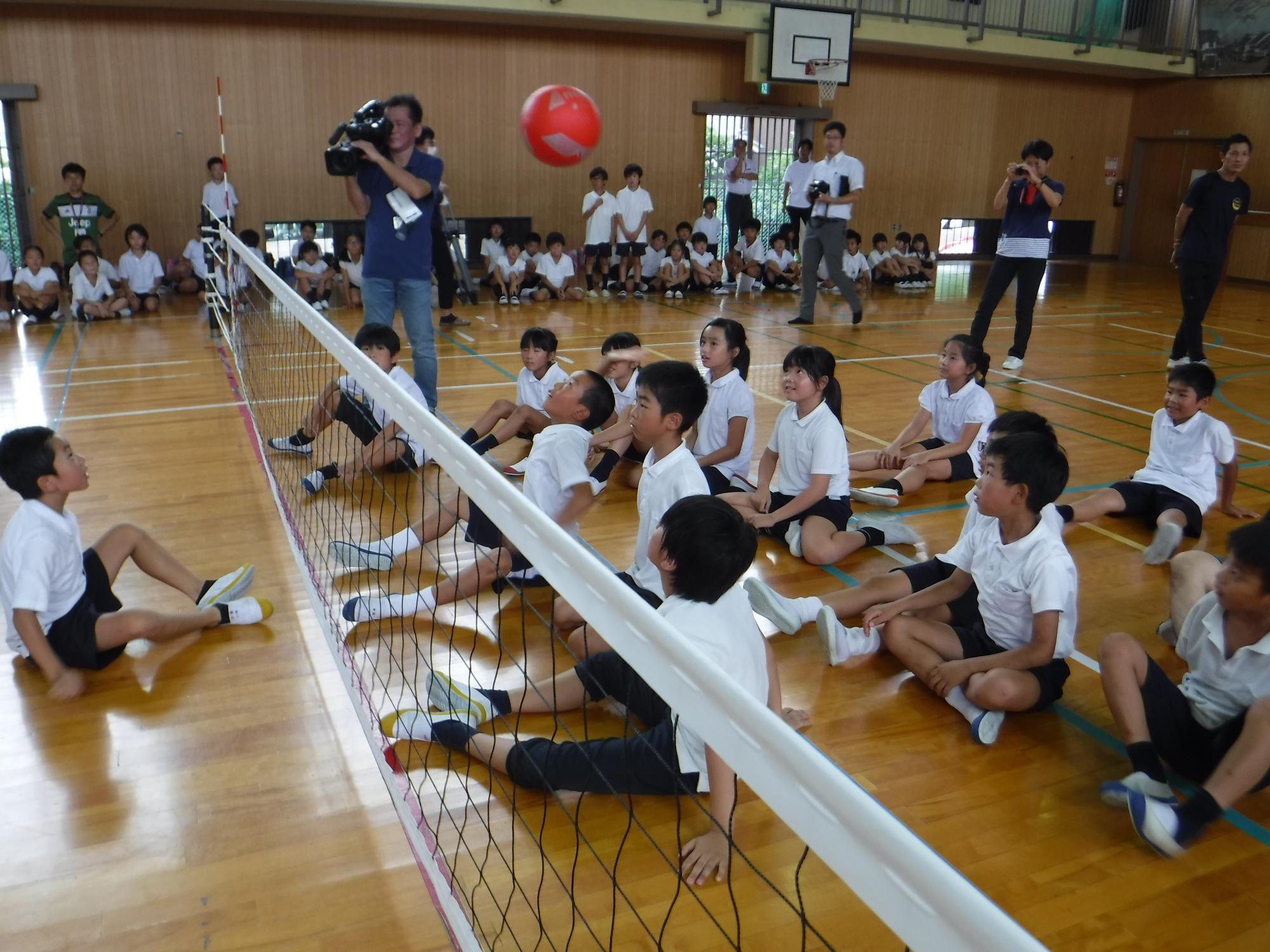 生徒が体育館でシッティングバレーボール体験を行っている写真