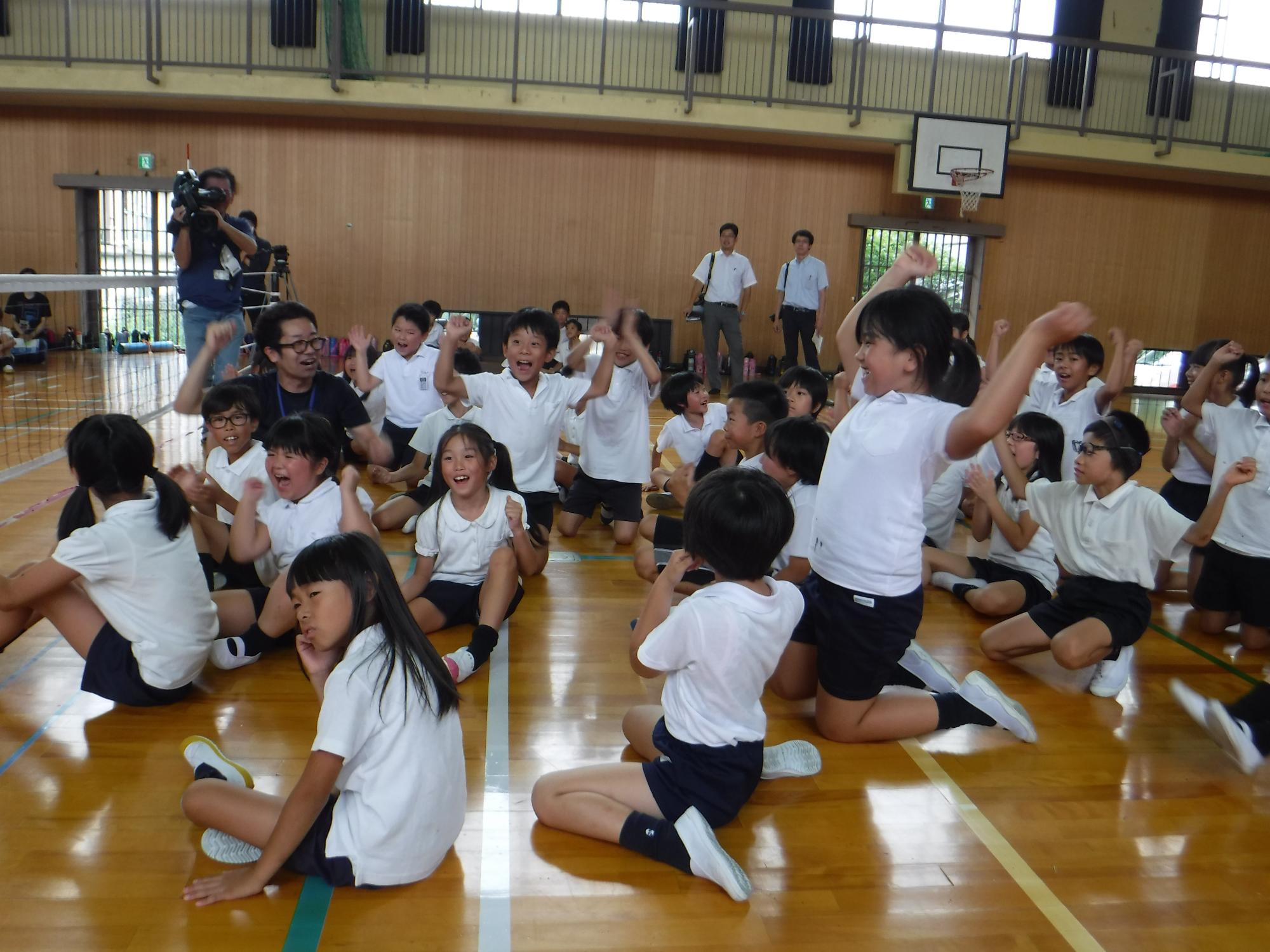 体育館でシッティングバレーボールを行う生徒が喜んでいる写真