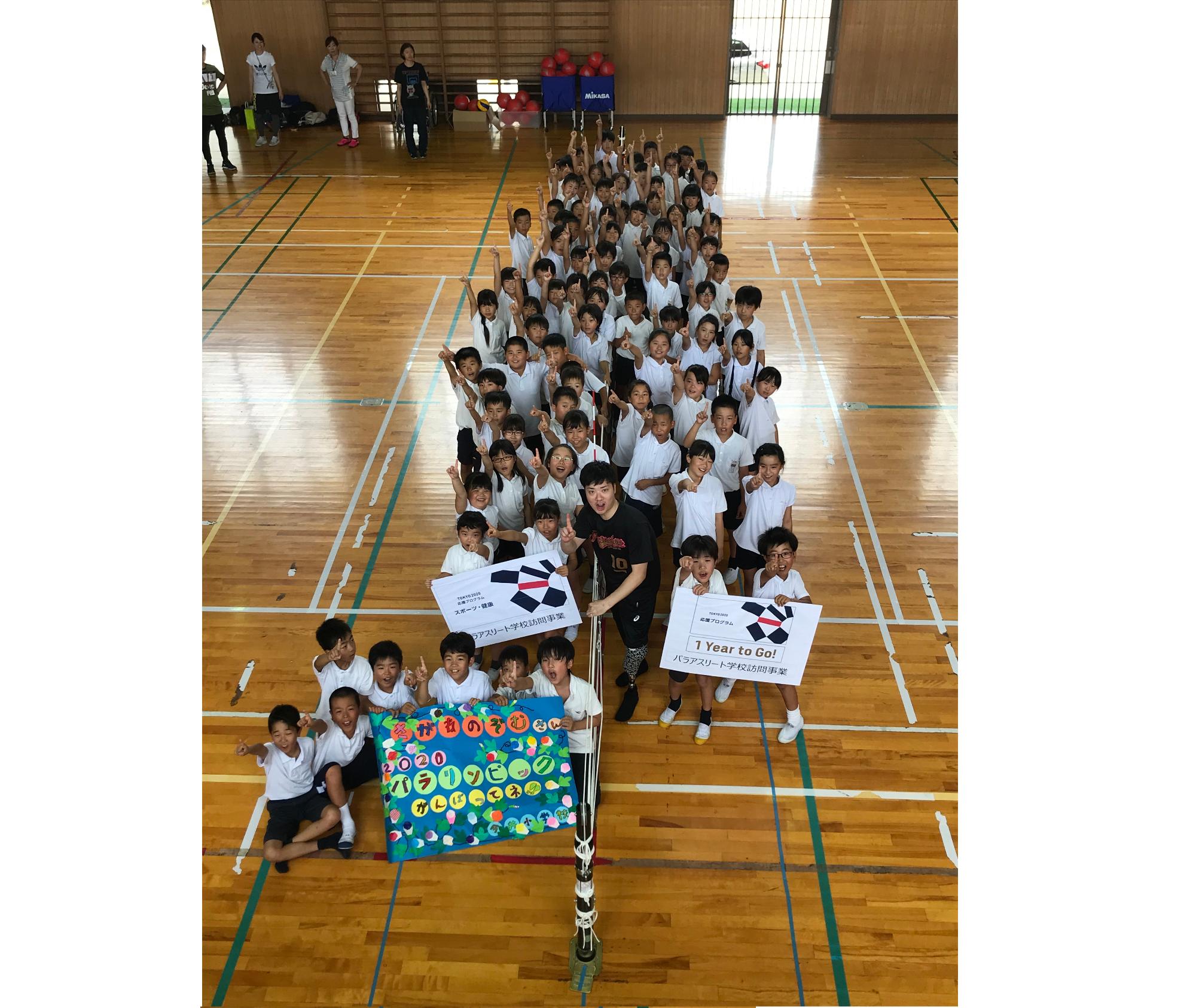 嵯峨根選手と生徒が体育館で数字の1を人文字で表現している集合写真