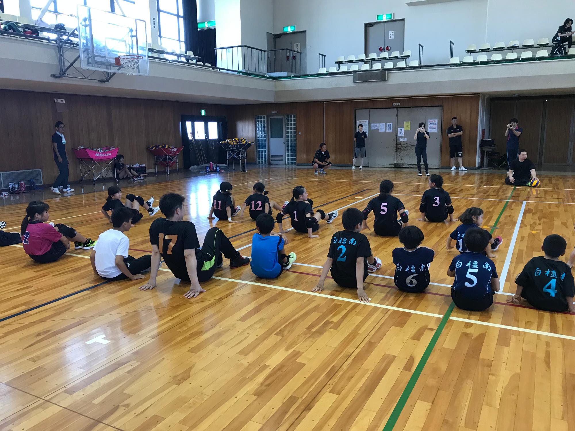 選手が体育館で座っている生徒にシッティングバレーボールびついて説明をしている写真