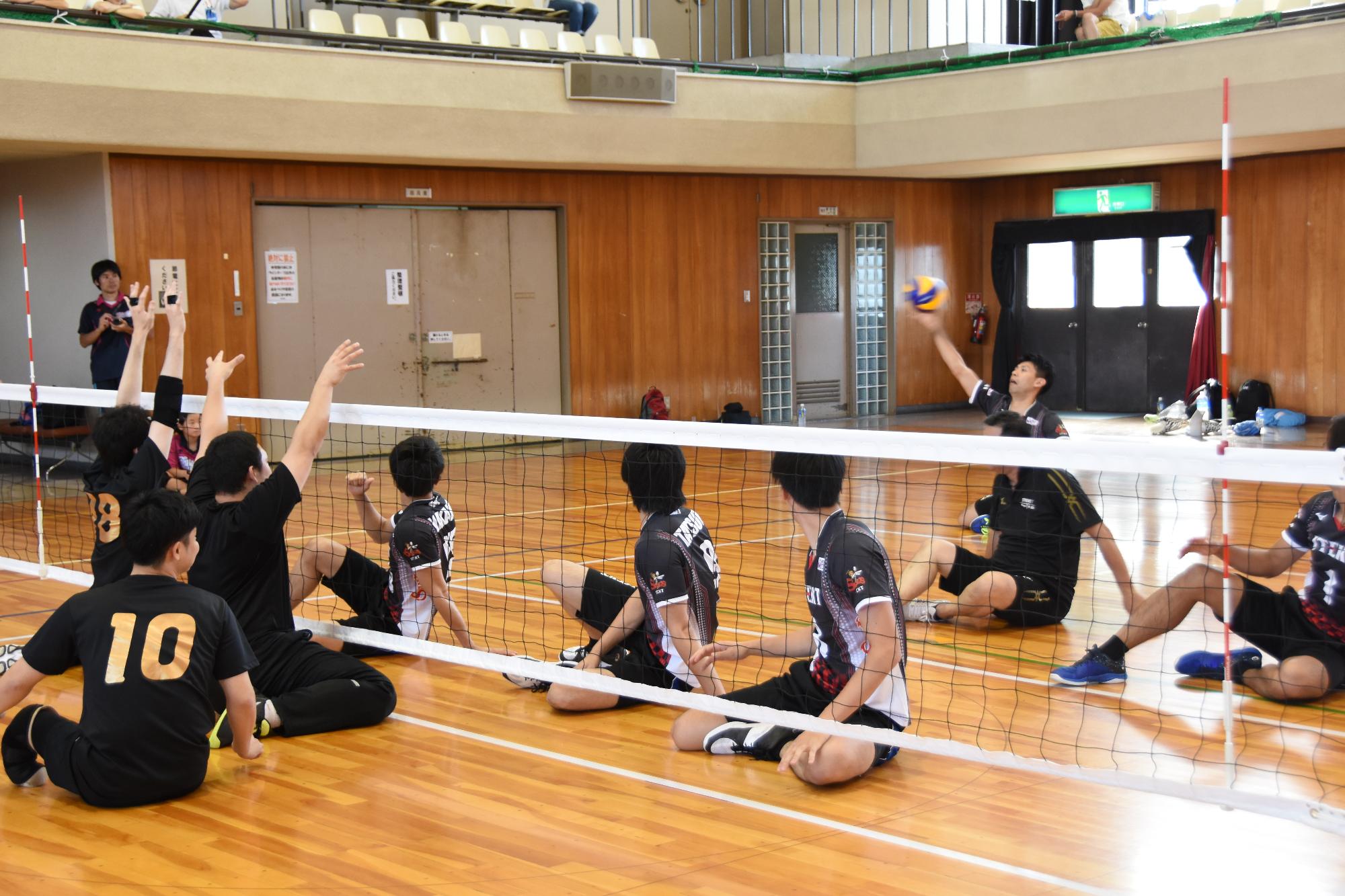 生徒がネット越しにバレーボールに手を伸ばしている写真