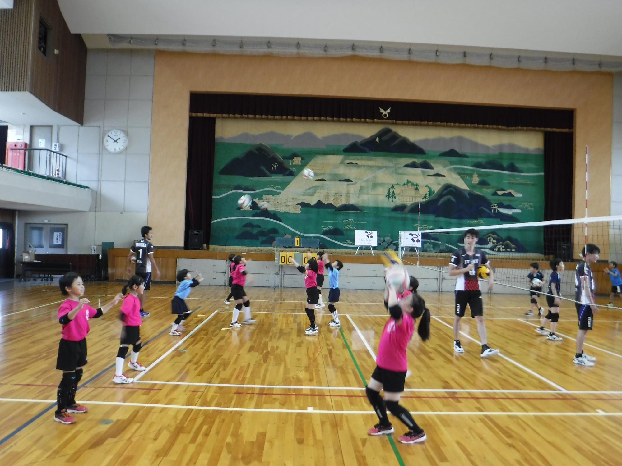 選手と生徒が体育館でバレーボールをしている写真