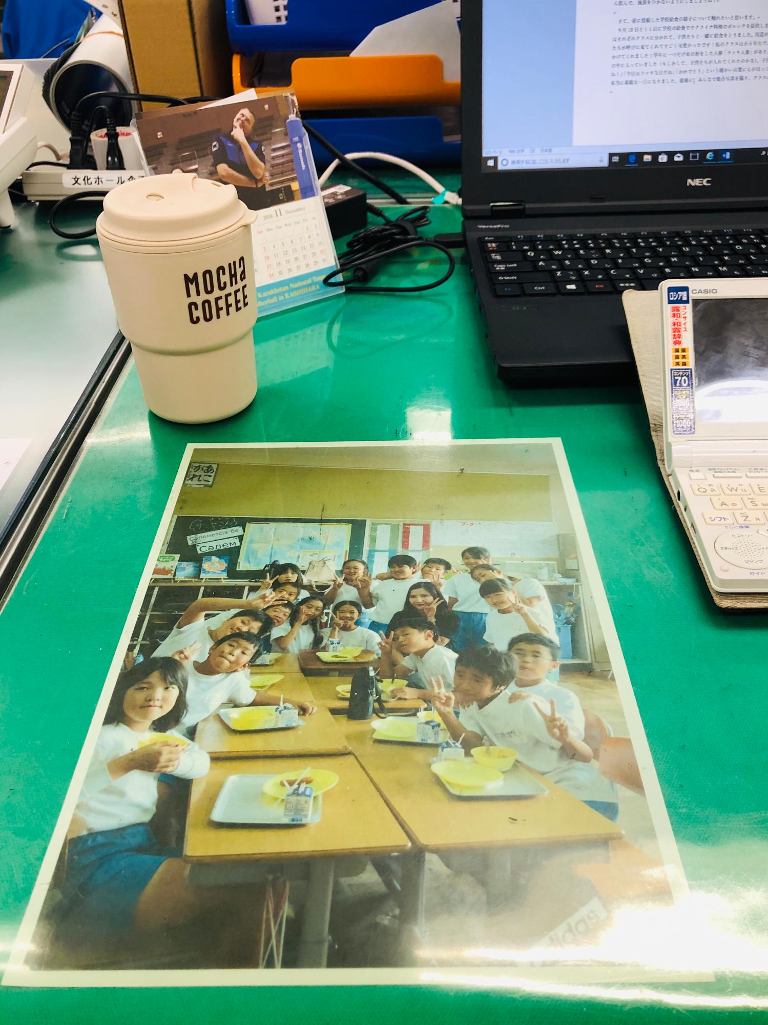 印刷された子供たちの集合写真が飾られた職場のデスクの写真