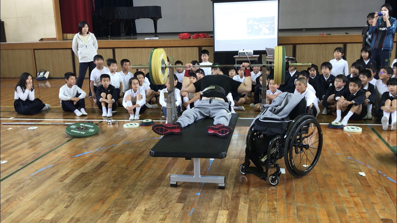 車椅子の男性選手が台の上でパワーリフティングをしている写真