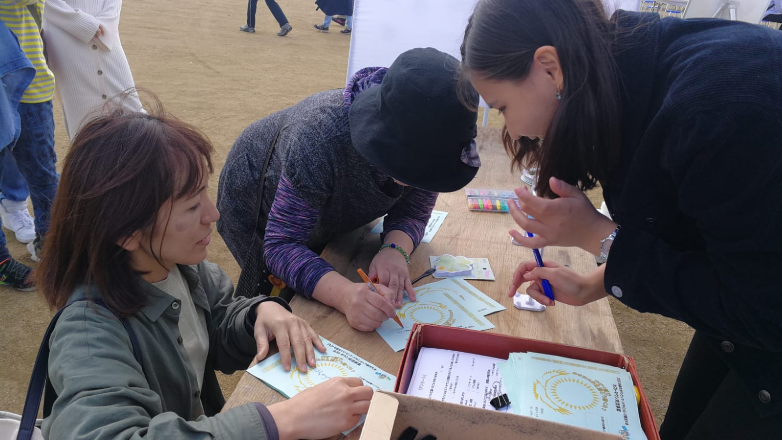 イベント会場のテーブルの上で紙にカザフ語で日本人女性の名前を書いているカザフスタンの女性の写真