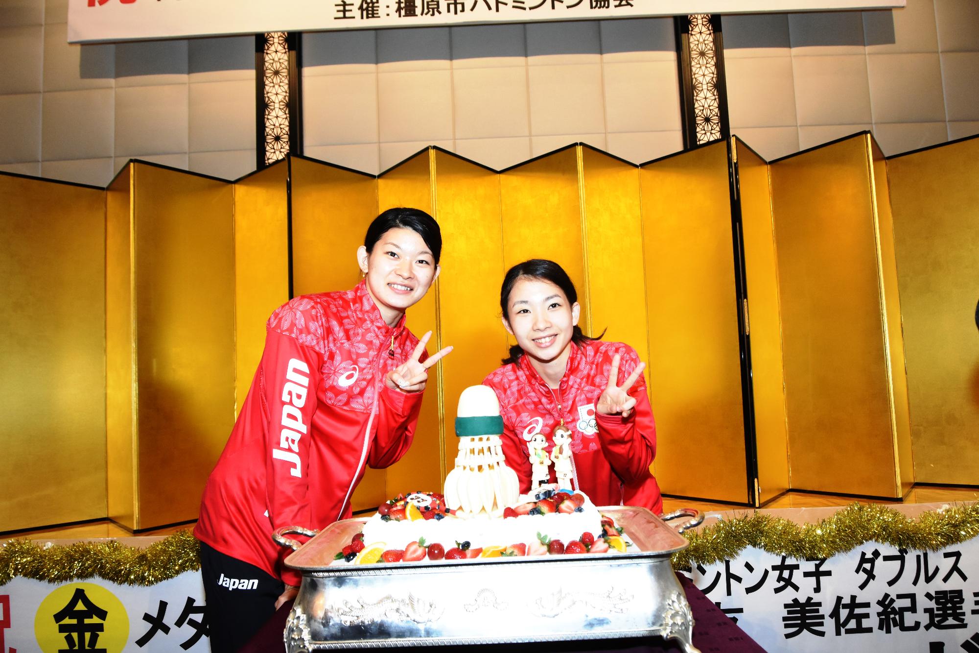 祝賀会でケーキを前にして手をピースにしている選手2人の写真