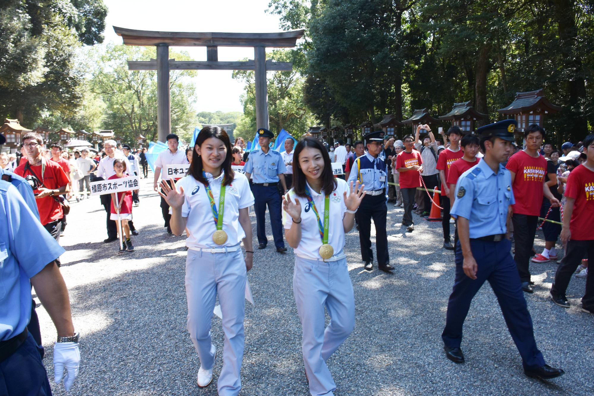 神社の参道を手を振りながら歩いている高橋選手と松友選手の写真