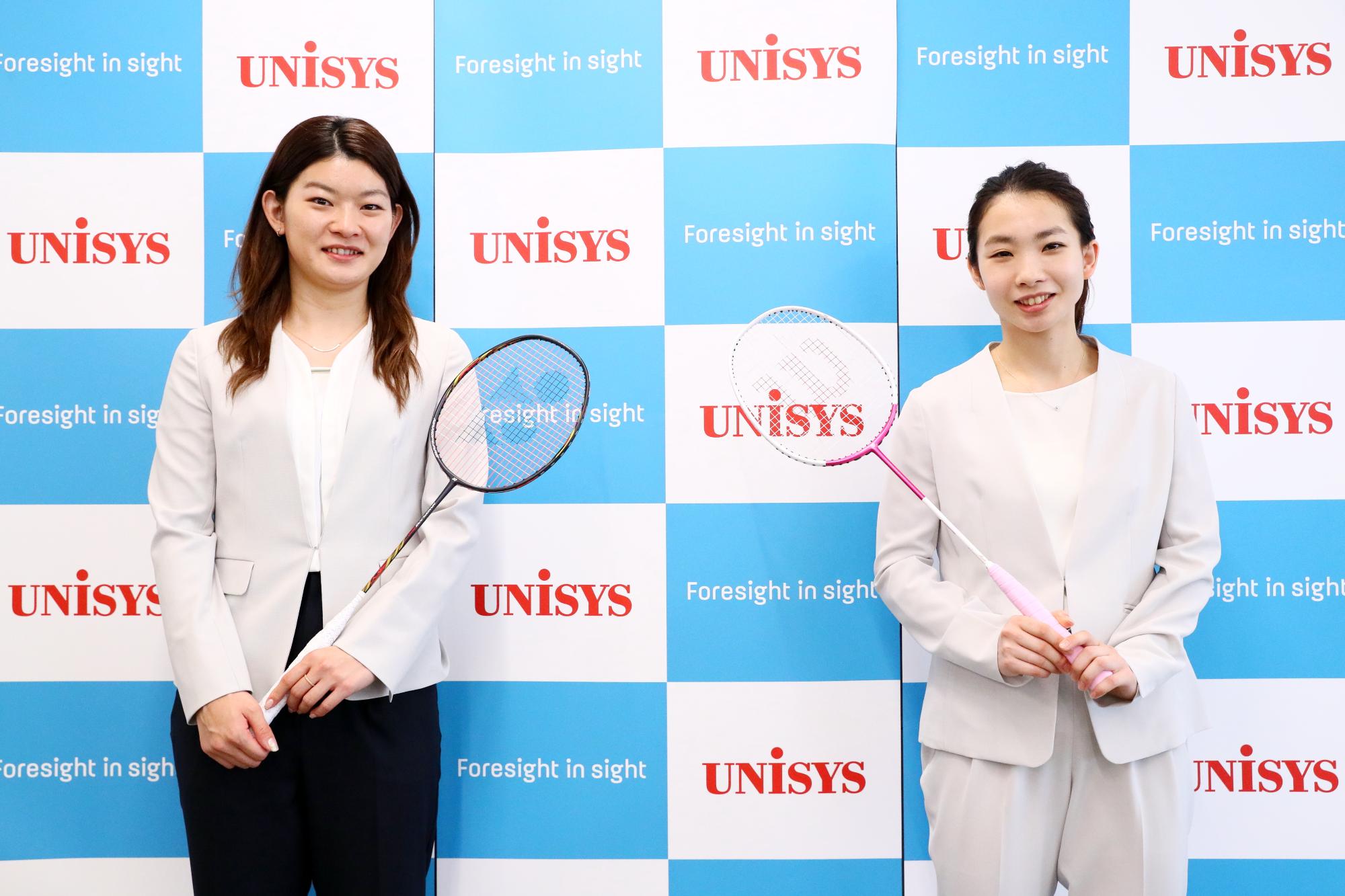 パネルの前でラケットを手に持ち笑顔の選手2人の写真