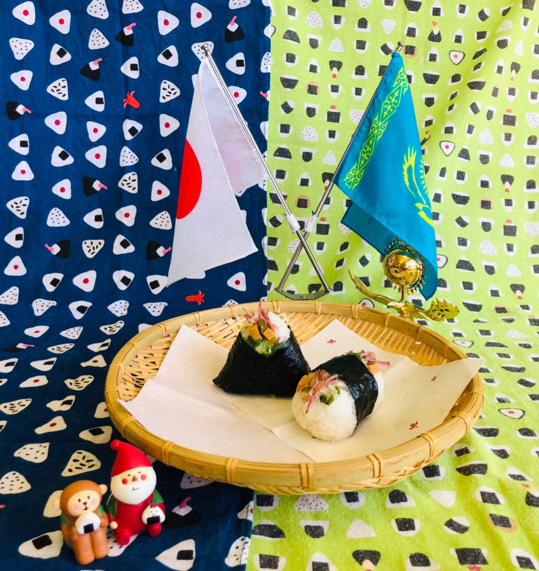 日本とカザフスタンの国旗が立ててあるザルの上に飛鳥さくらにぎりが二つ置いてある写真