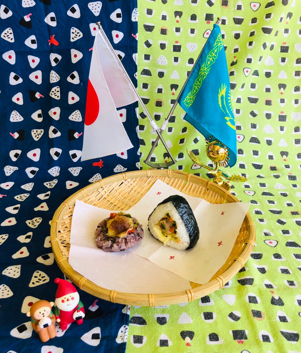 日本とカザフスタンの国旗が立ててあるザルの上にいろ鶏どりにぎりが二つ置いてある写真
