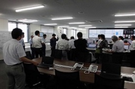広域消防組合の室内で立って研修を受ける議員達の写真