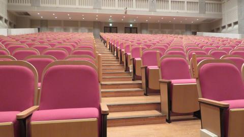 通路側の背もたれに手かけ棒が設置された会場内座席の写真