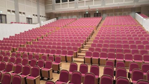 通路側の背もたれに手かけ棒が設置された会場内座席の全体写真