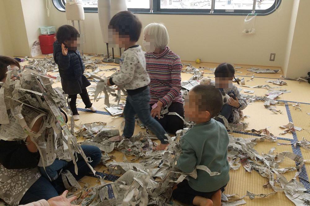 細長く切り刻んだ新聞ではしゃぐ幼児達の写真