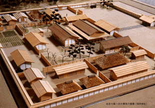 長方形に仕切られた塀の中の敷地に、多数の長屋建築と、畑や樹木などを再現した模型の写真。