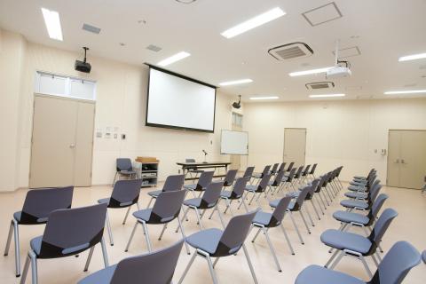 天井からスクリーンが吊るされていて、椅子が並べられている室内の写真