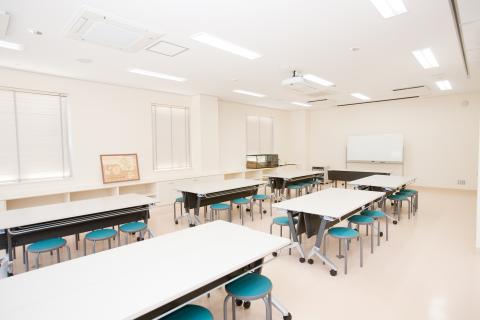 ホワイトボードと、長机が6つ、それぞれ丸椅子が6つ用意されている研修室の写真