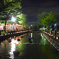 夜の川沿いを灯火が照らしている様子を撮影した写真