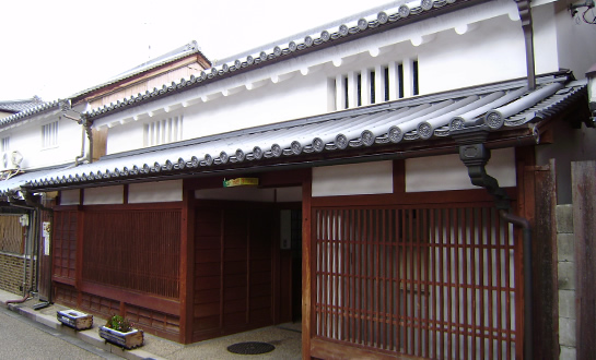 木製の格子が掛けられた白い壁の瓦屋根住居の写真