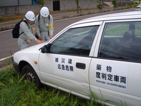 二人の作業員が白い車に防災関連のステッカーを貼っている写真